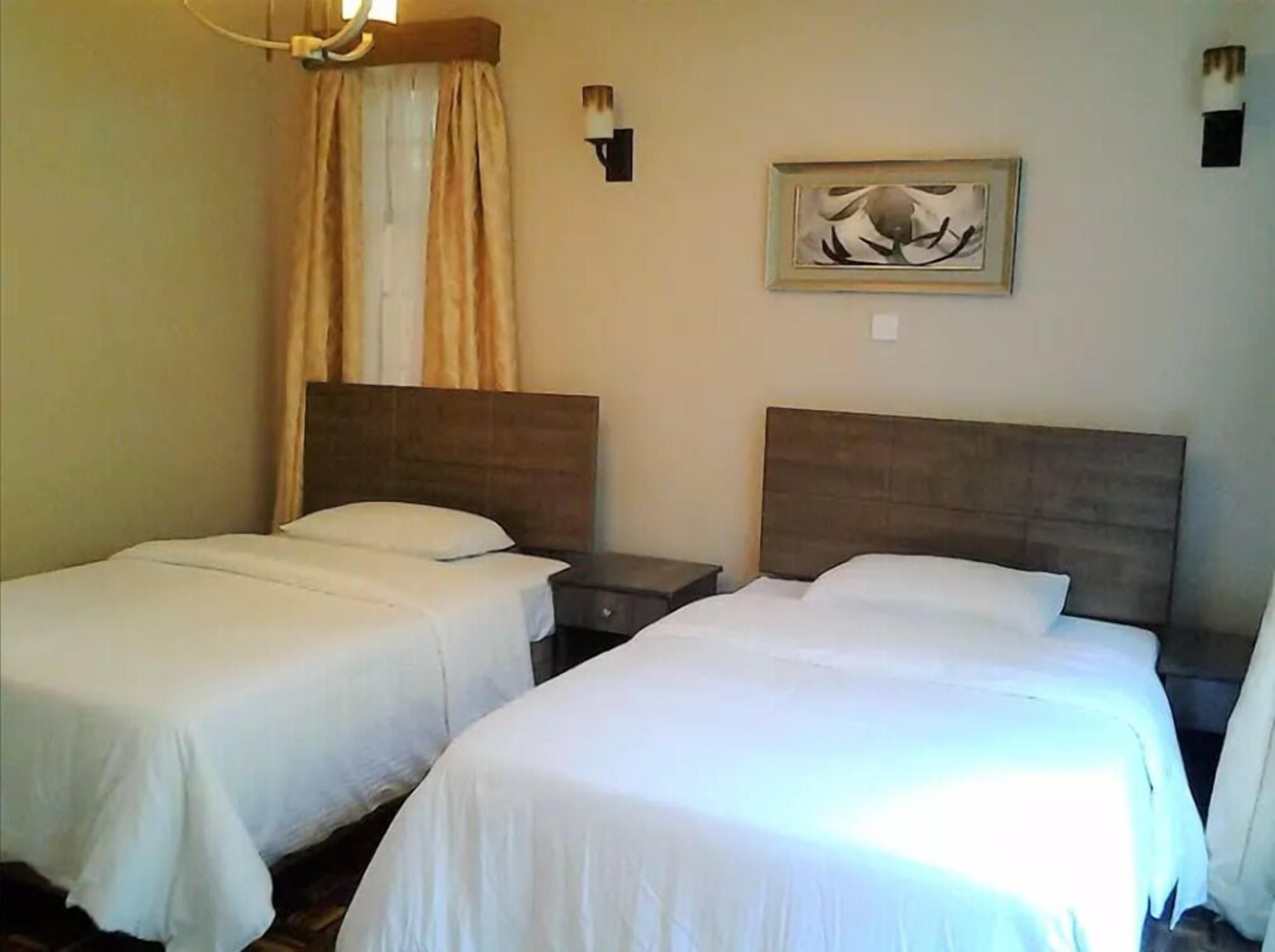 Habitación de hotel con dos camas individuales, una mesita de noche, una lámpara, un cuadro y una ventana con cortinas.