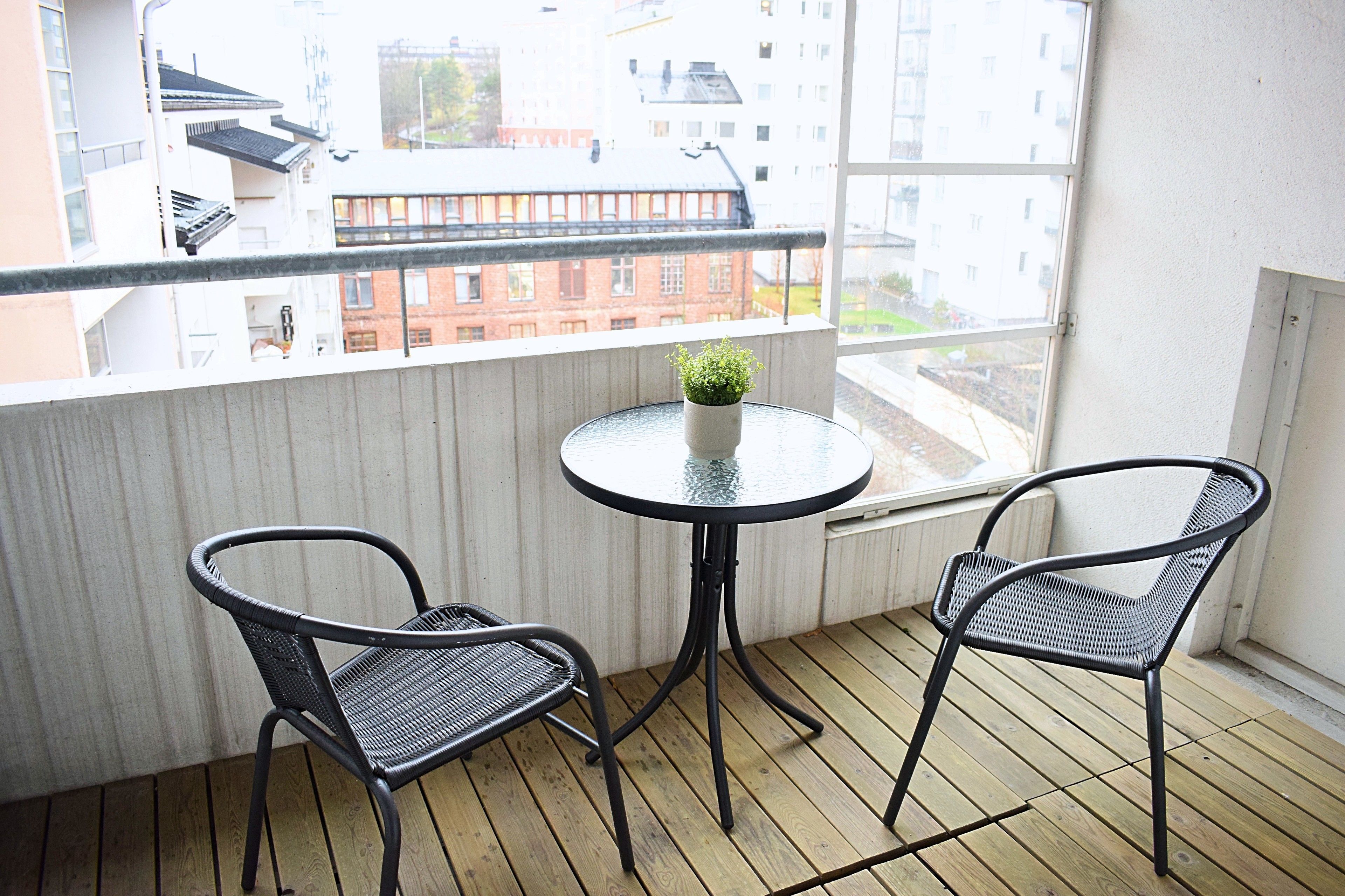 A balcony with two chairs and a small table, overlooking a cityscape.