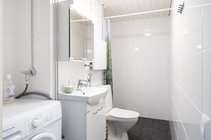A modern bathroom with a built-in washer and dryer, a sink, and a toilet. - Hiisi Homes Helsinki Sörnäinen (Helsinki)