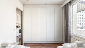 Une chambre d’hôtel avec un plancher en bois, un lit avec du linge de maison blanc, une armoire et une fenêtre avec des rideaux.
