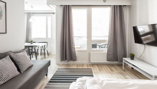 Une chambre d’hôtel moderne dotée d’un canapé, d’une télévision, d’un coin repas et d’un balcon avec des rideaux.