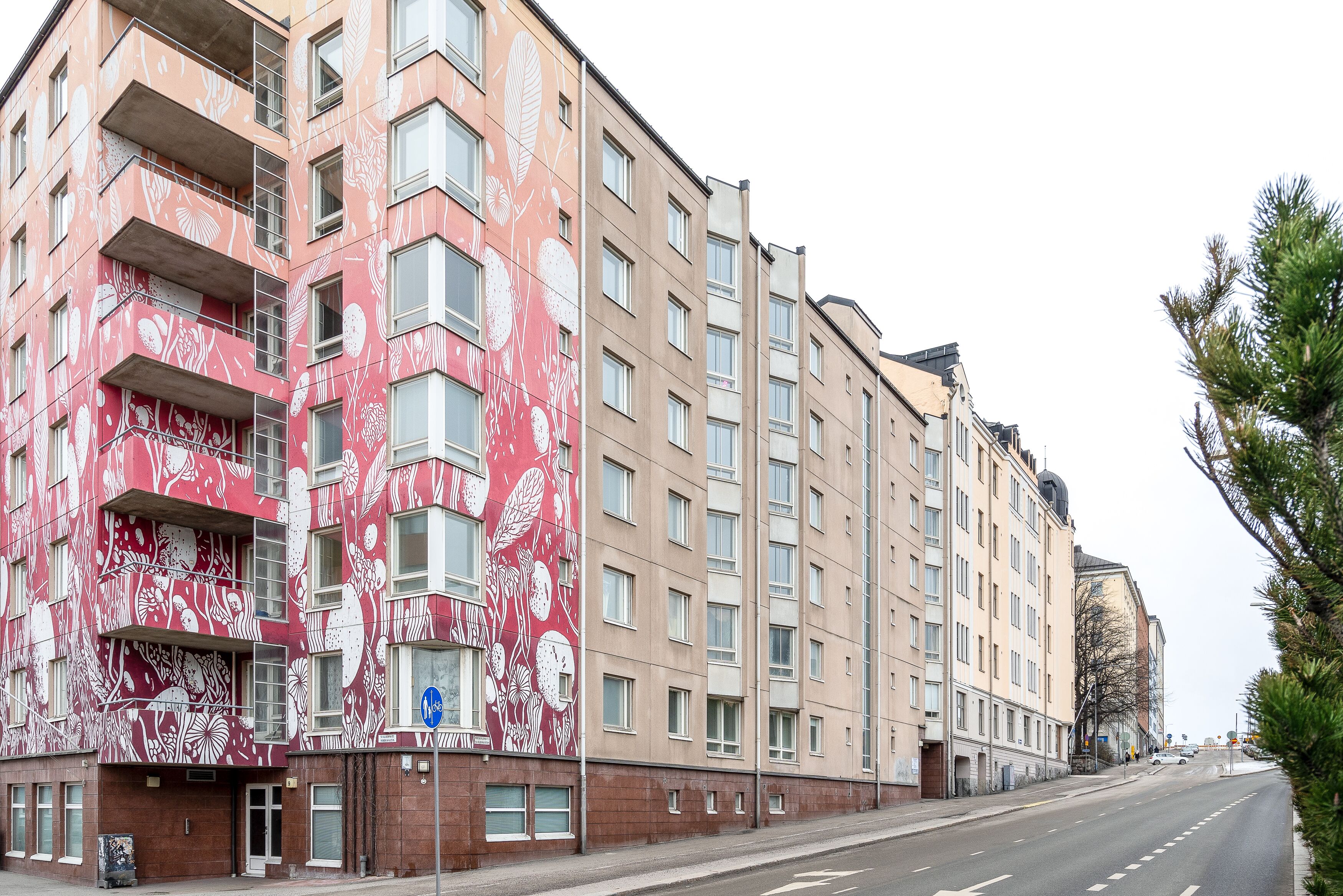 A multi-story building with a distinctive red and white floral facade, multiple balconies, and a clear street view.