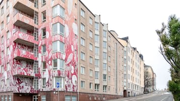 A multi-story building with a distinctive red and white floral facade, multiple balconies, and a clear street view.