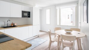 Une cuisine moderne avec des meubles blancs, un micro-ondes noir et une table à manger en bois, accompagnée de chaises.
