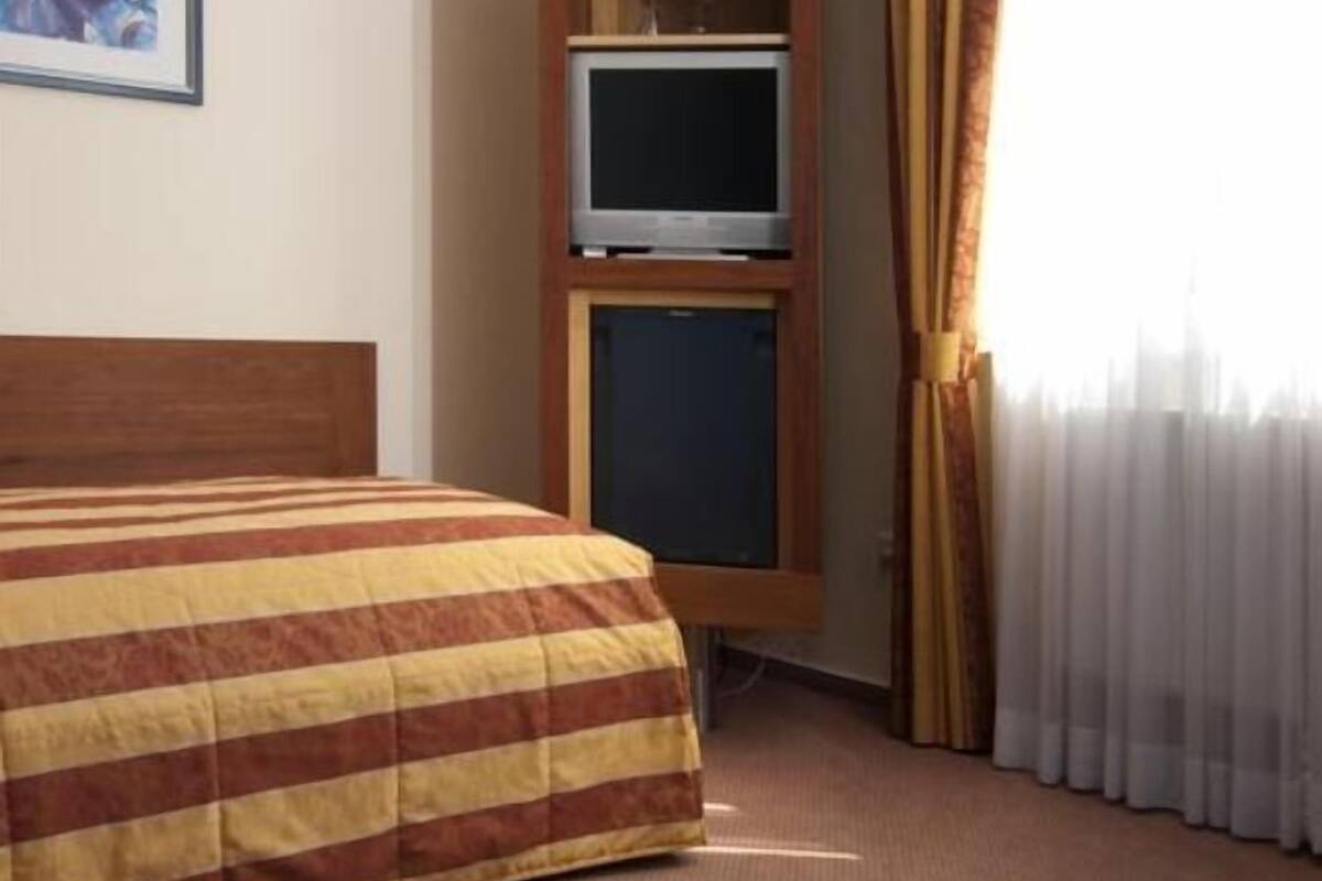 A hotel room with a bed, a television on a wooden stand, and a window with curtains.