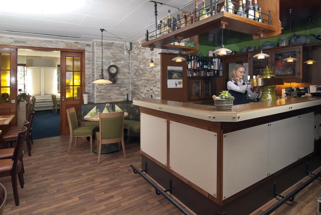 Eine Bar mit Bartender, einer Holztresen und Regalen mit Flaschen. Angrenzend befindet sich ein Essbereich mit Stühlen und Tischen.