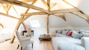 A loft-style room with exposed wooden beams, a light-colored sofa, a chair, and a coffee table. - L'Ecrin des Vignes (Sermiers)
