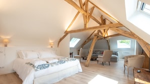 A bedroom with a sloped ceiling, wooden beams, a bed, a desk, and a chair. - L'Ecrin des Vignes (Sermiers)