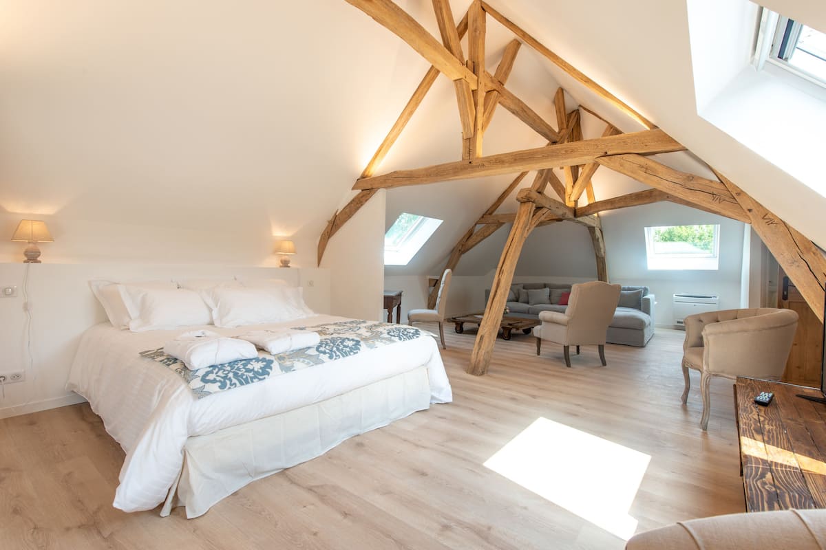 Un dormitorio con techo inclinado, vigas de madera, cama, escritorio y silla.