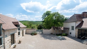 A courtyard with stone buildings, a gravel path, and a view of green fields. - L'Ecrin des Vignes (Sermiers)