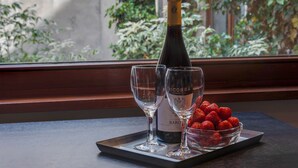A bottle of wine, two glasses, and a bowl of strawberries on a tray by a window with a view of greenery. - EUROPEA Residence Grande Place Brussels (Brussels)