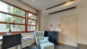 A modern room with a large window, a chair, a small table, a cabinet, and a door. - EUROPEA Residence Grande Place Brussels (Brussels)
