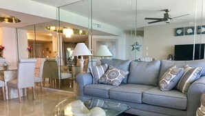 Ein modernes Wohnzimmer mit einem grauen Sofa, gemusterten Kissen, einem Glastisch und einer Steinsäule.