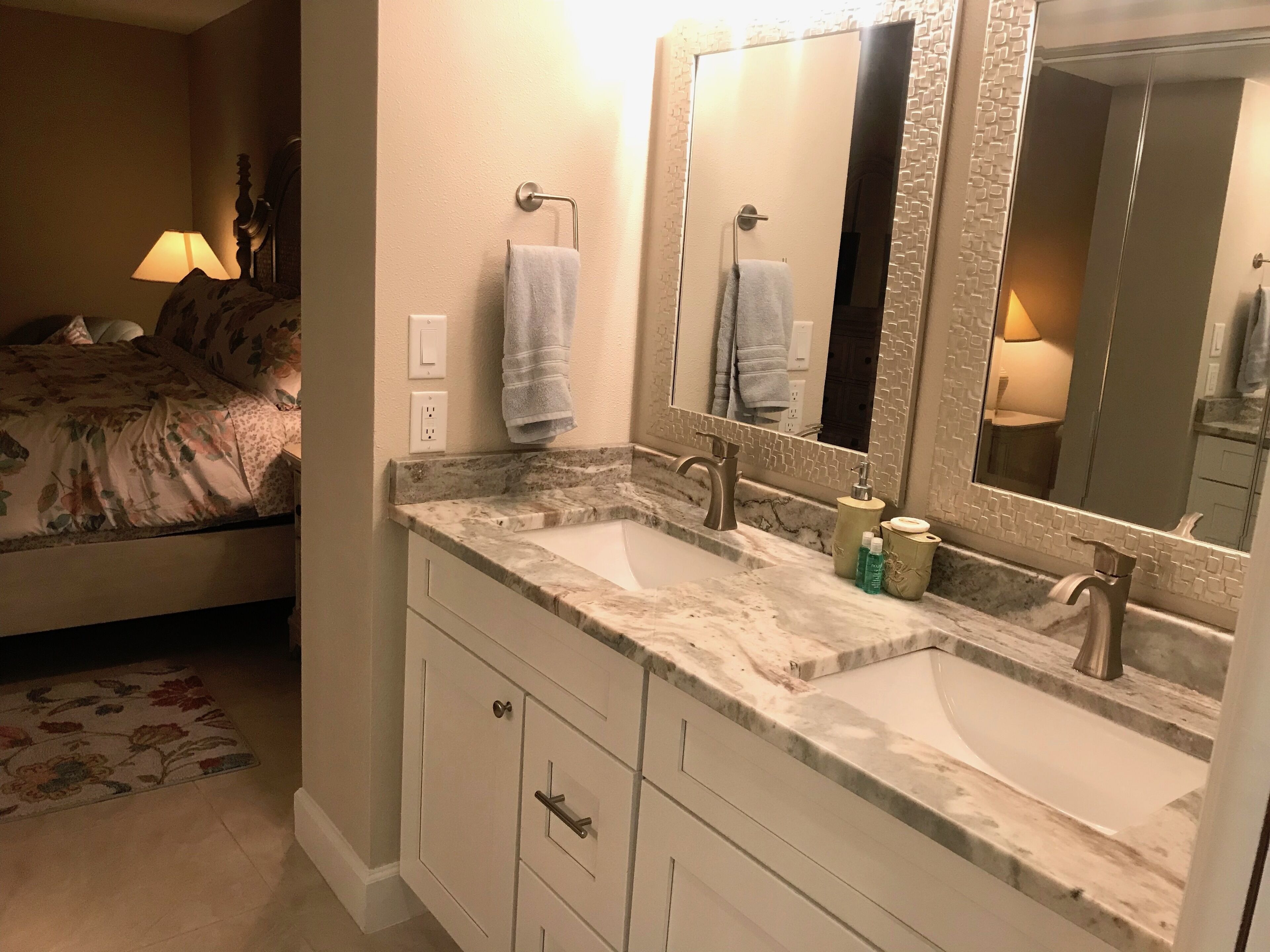 Une salle de bain avec deux lavabos, un grand miroir et un lit avec une literie à motifs floraux.