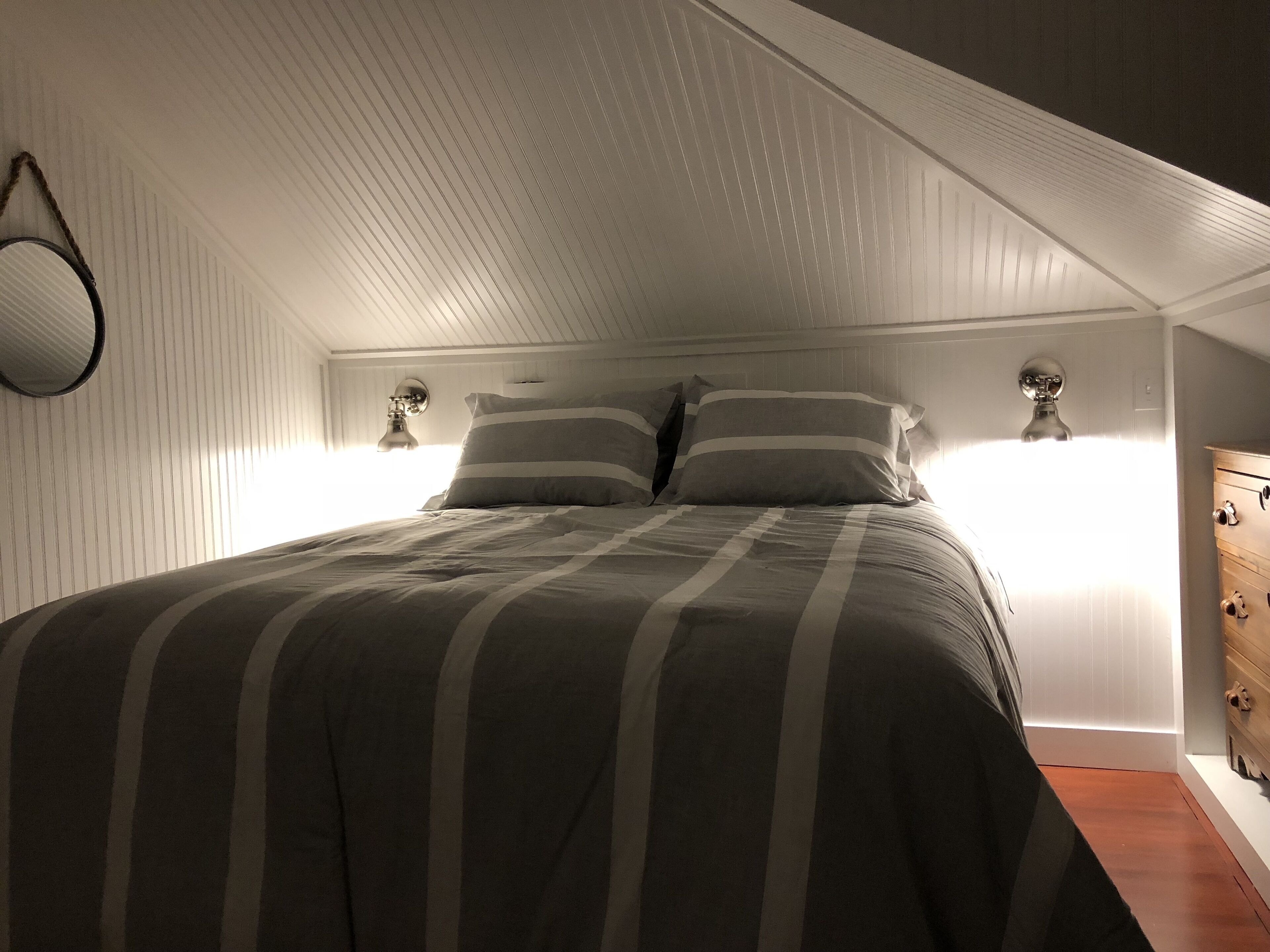 A bedroom with a bed, two bedside lamps, a dresser, and a sloped ceiling.