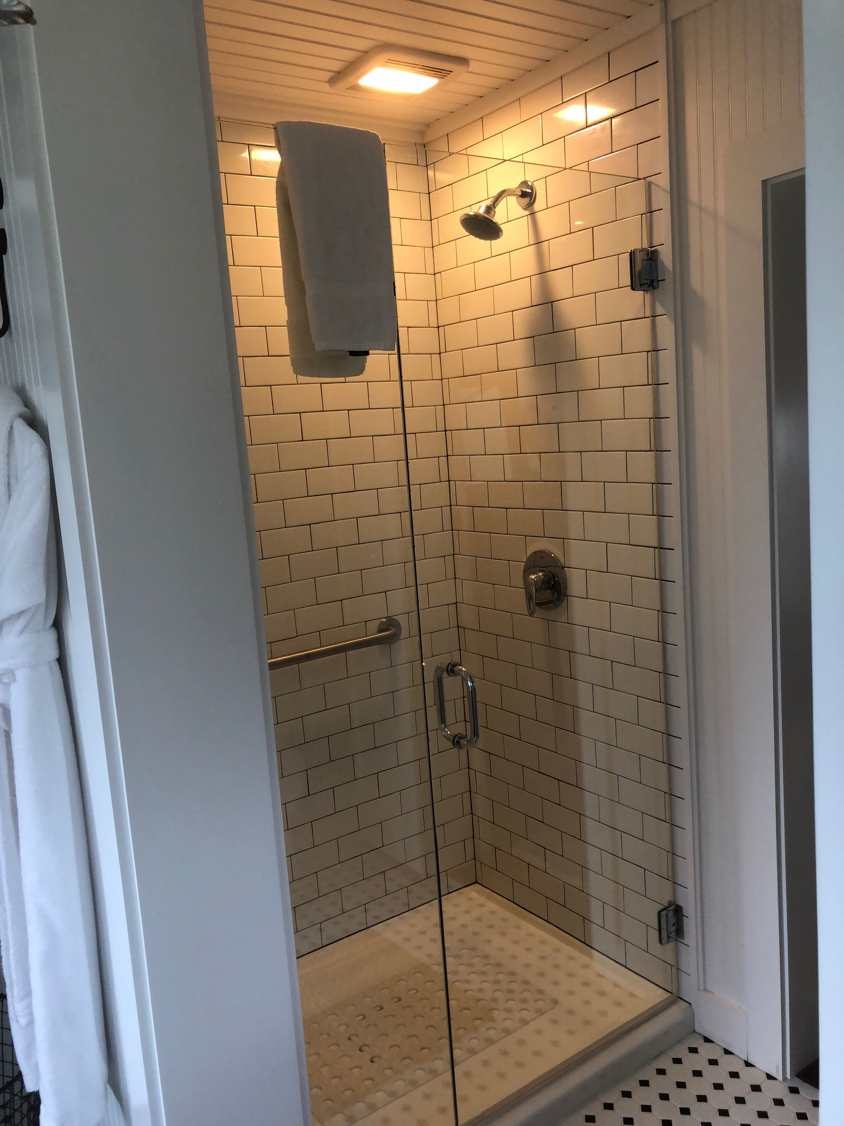 A glass-enclosed shower with beige tiles, a towel hanging on the wall, and a metal grab bar.