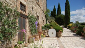 A stone building with a garden pathway, potted plants, and a large stone wheel. - Agriturismo Casale dei Frontini (Todi)