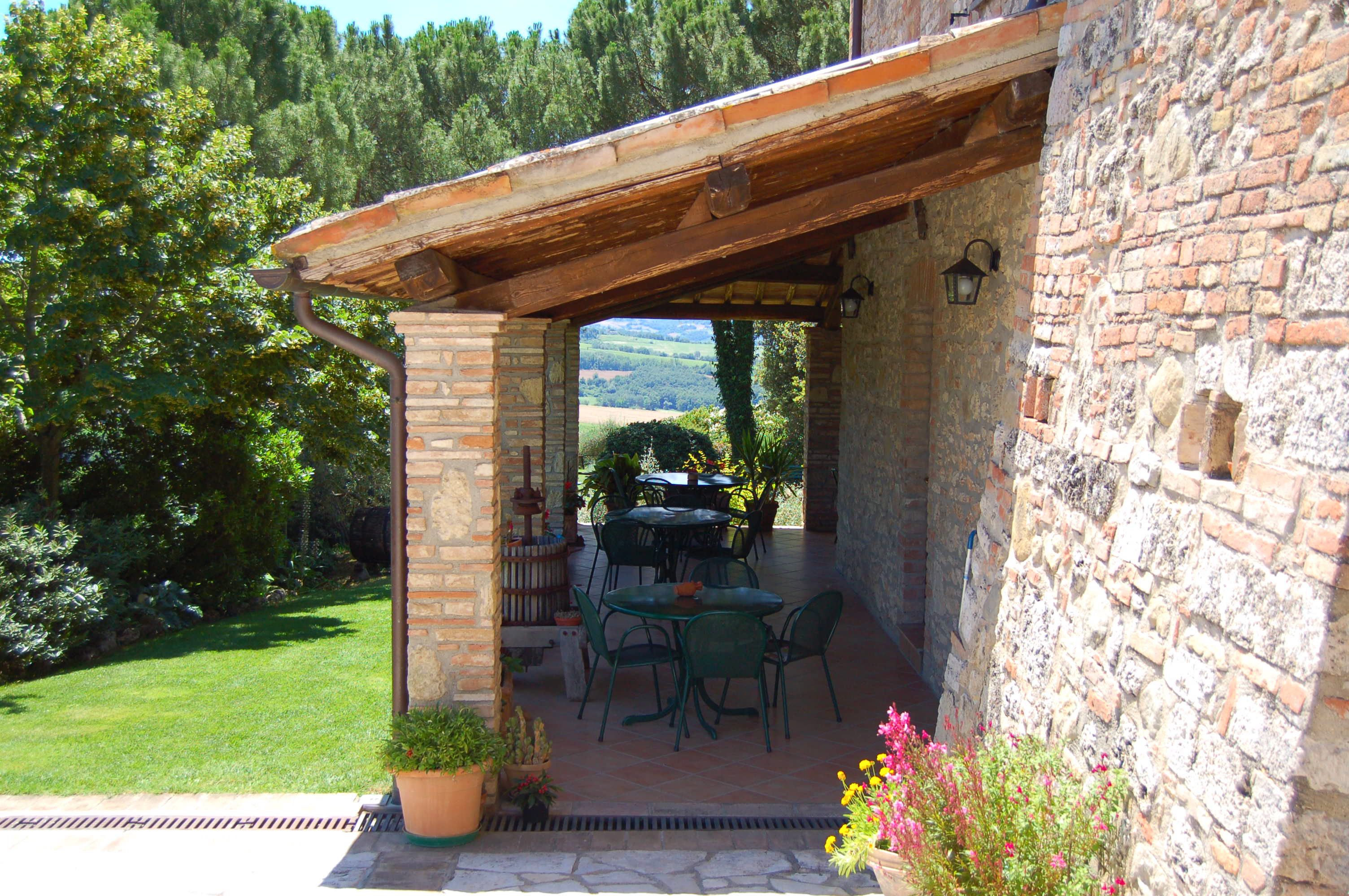 Een stenen gebouw met een houten pergola, terras en uitzicht op het platteland.