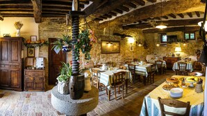 A rustic dining area with stone walls, wooden beams, and traditional decor. Tables are set with plates and cutlery, and there are potted plants and a large vase with flowers. - Agriturismo Casale dei Frontini (Todi)