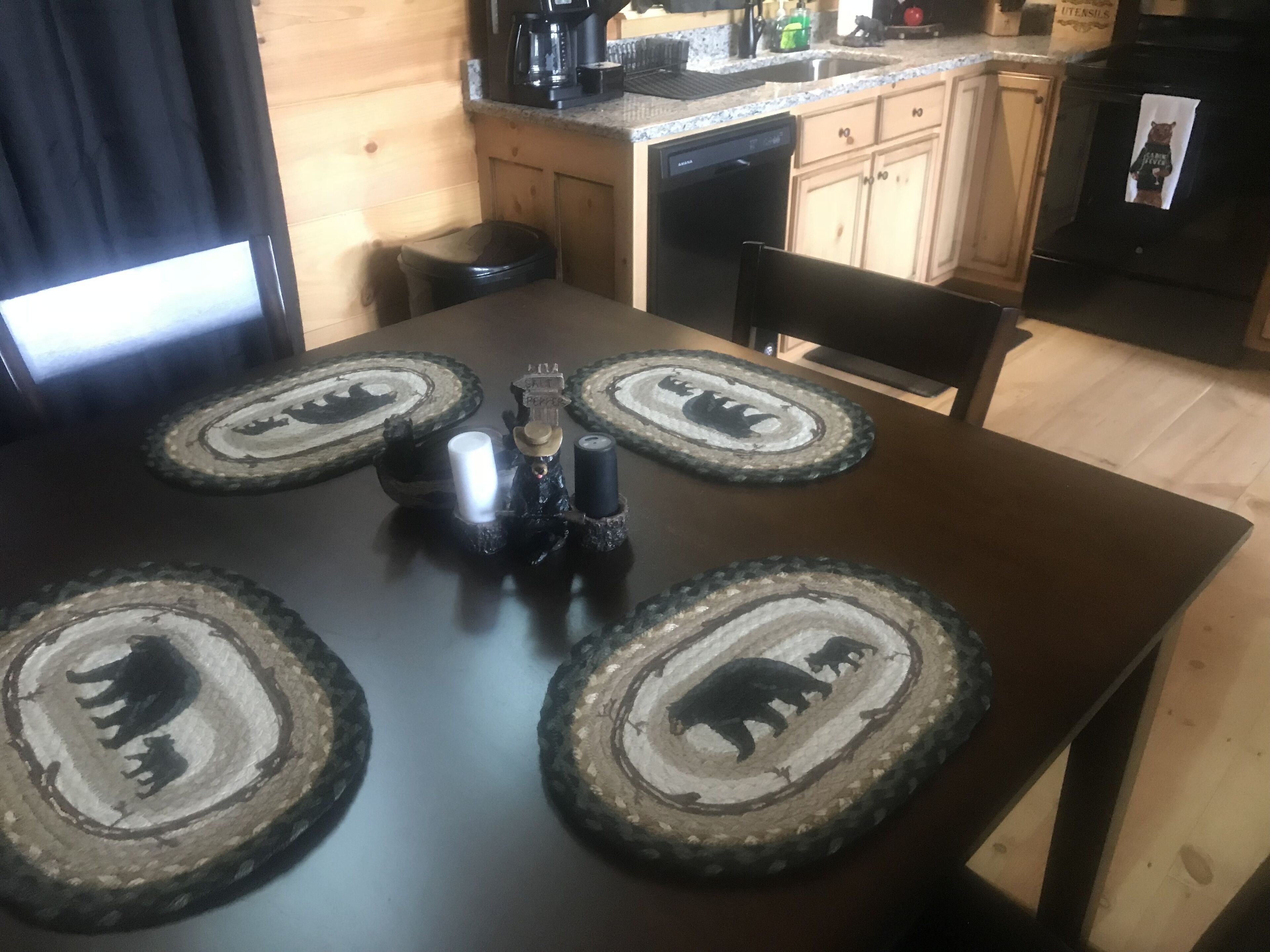 Una mesa de comedor de madera con cuatro posavasos con diseños de osos, un candelabro negro y un pequeño adorno.