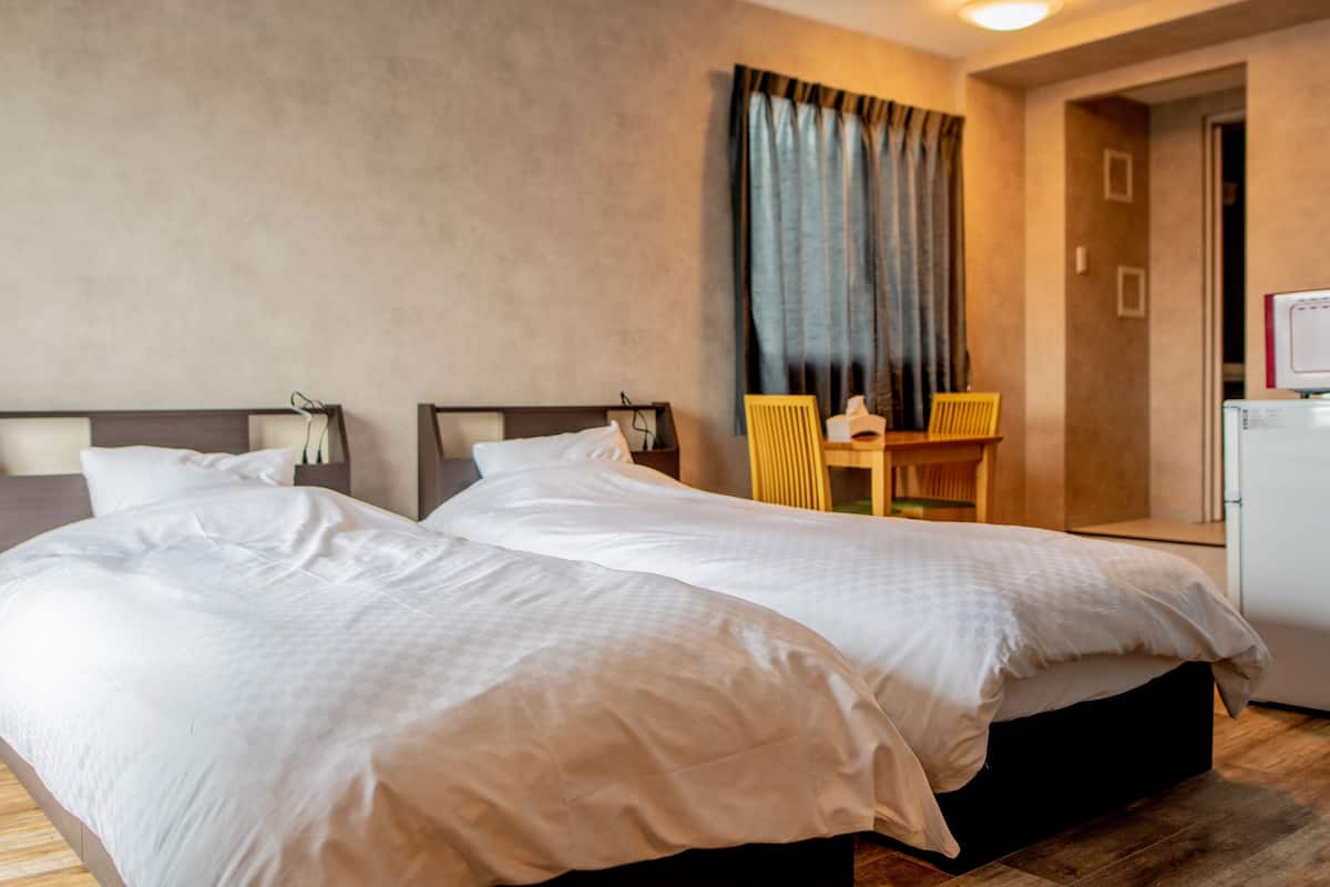 A hotel room with two beds, a desk, a chair, and a small kitchenette.