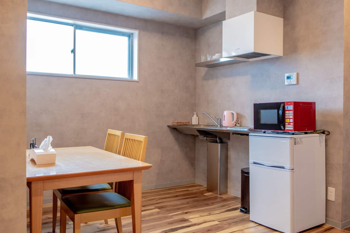 A compact kitchen with a wooden table, chairs, a white refrigerator, a microwave, and a window.