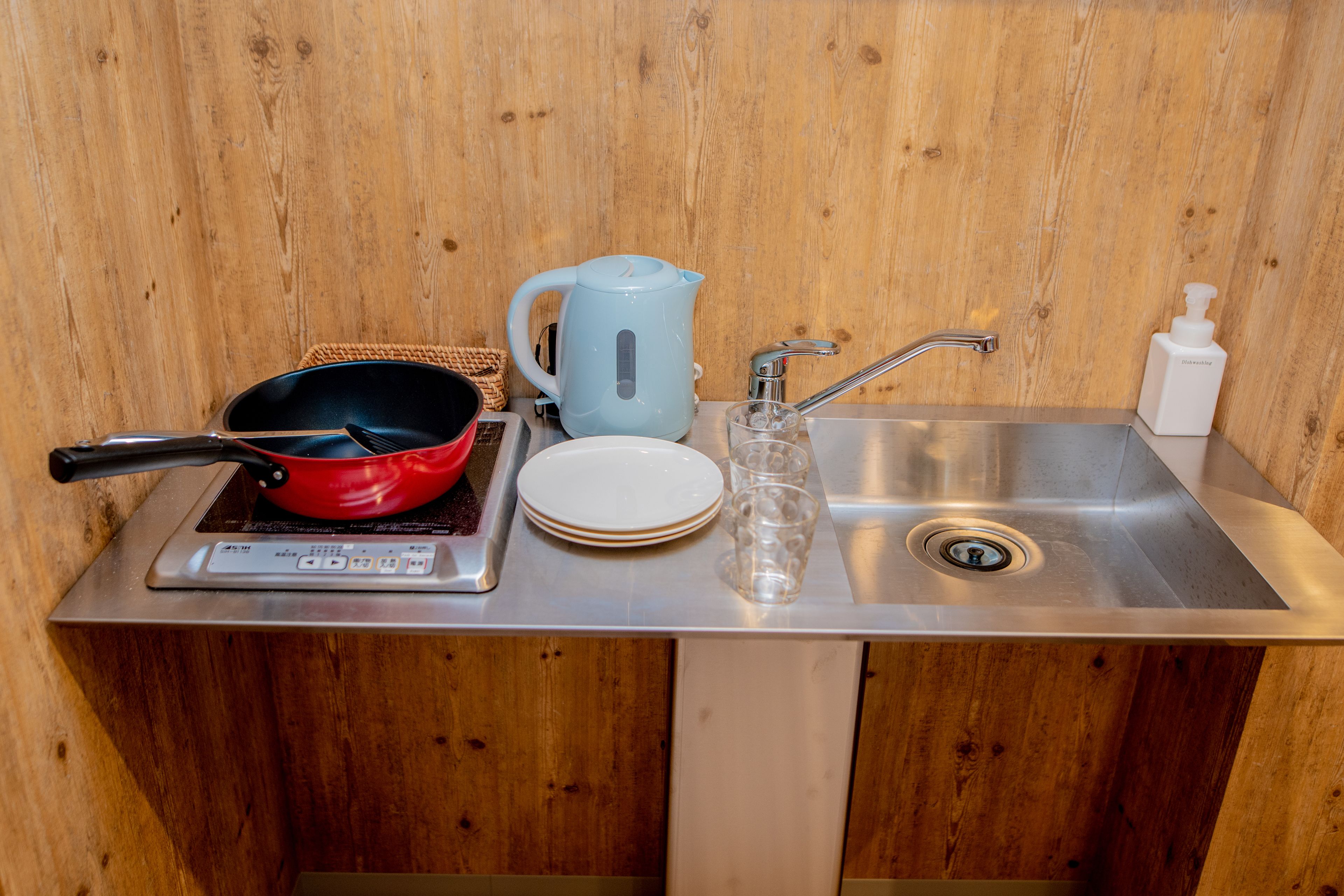 A kitchen area with a stove, a kettle, a sink, and a soap dispenser.