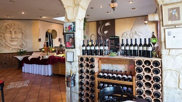 Una sala de cata de vinos con un arco de piedra, estanterías llenas de botellas y una mesa dispuesta para la degustación.