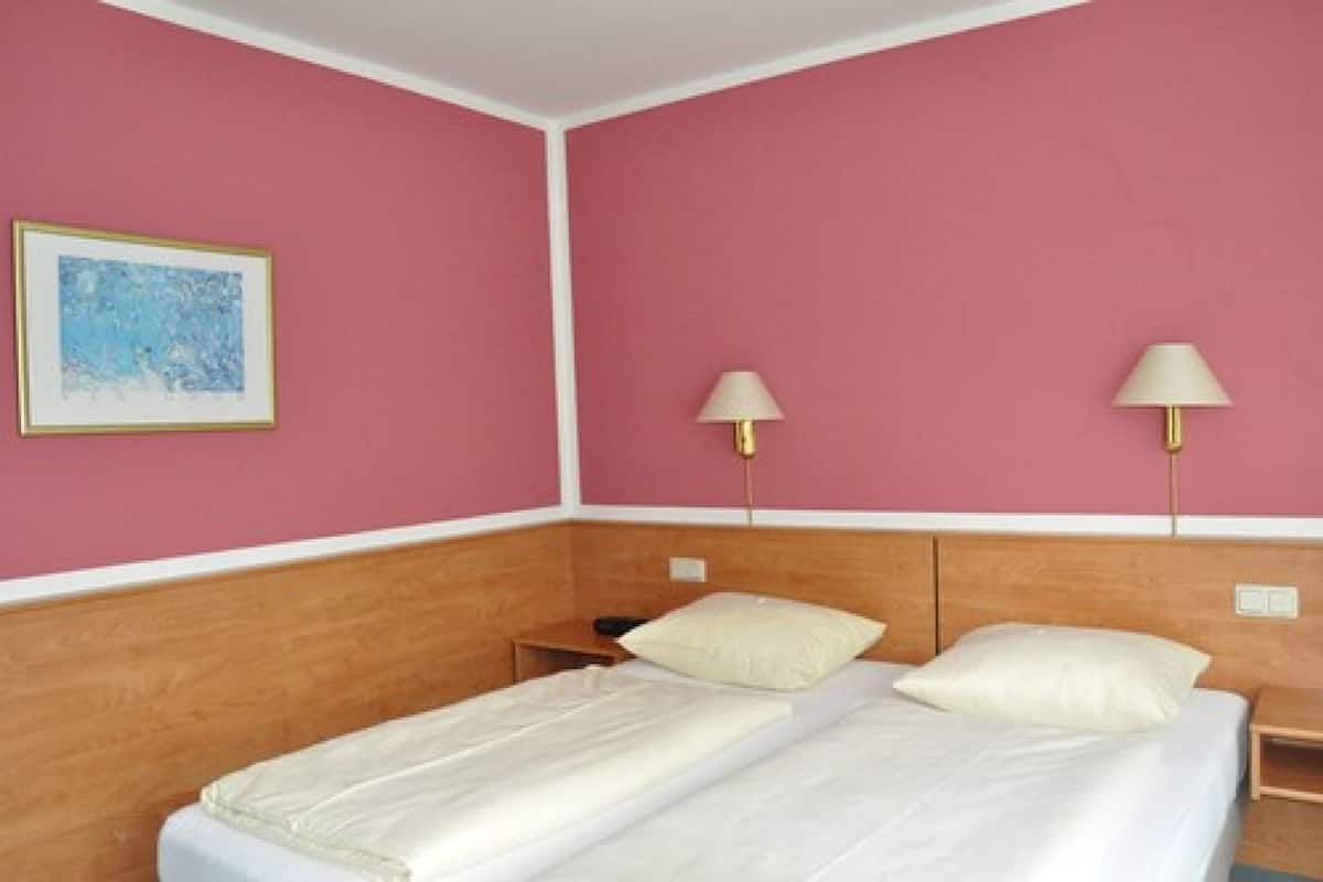 A hotel room with two beds, a wooden headboard, a pink wall, and two bedside lamps.
