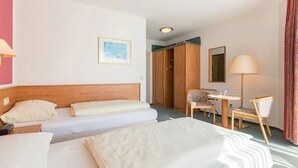 Habitación de hotel con dos camas, un escritorio, una silla, un armario y un espejo.