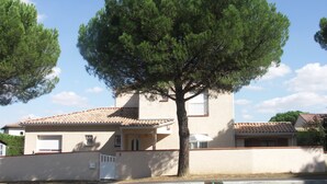 A two-story building with a tiled roof, a garage door, and a large tree in front. - Chambres d'Hôtes Le Saint Ô Détente (Saint-Orens-de-Gameville)