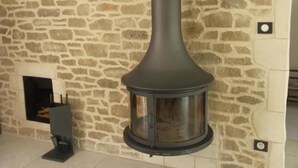 A stone wall with a fireplace and a modern, cylindrical wood stove. - Chambres d'Hôtes Le Saint Ô Détente (Saint-Orens-de-Gameville)