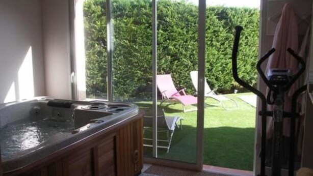 A room with a hot tub, a sliding glass door leading to a garden with chairs and a lawnmower. - Chambres d'Hôtes Le Saint Ô Détente (Saint-Orens-de-Gameville)