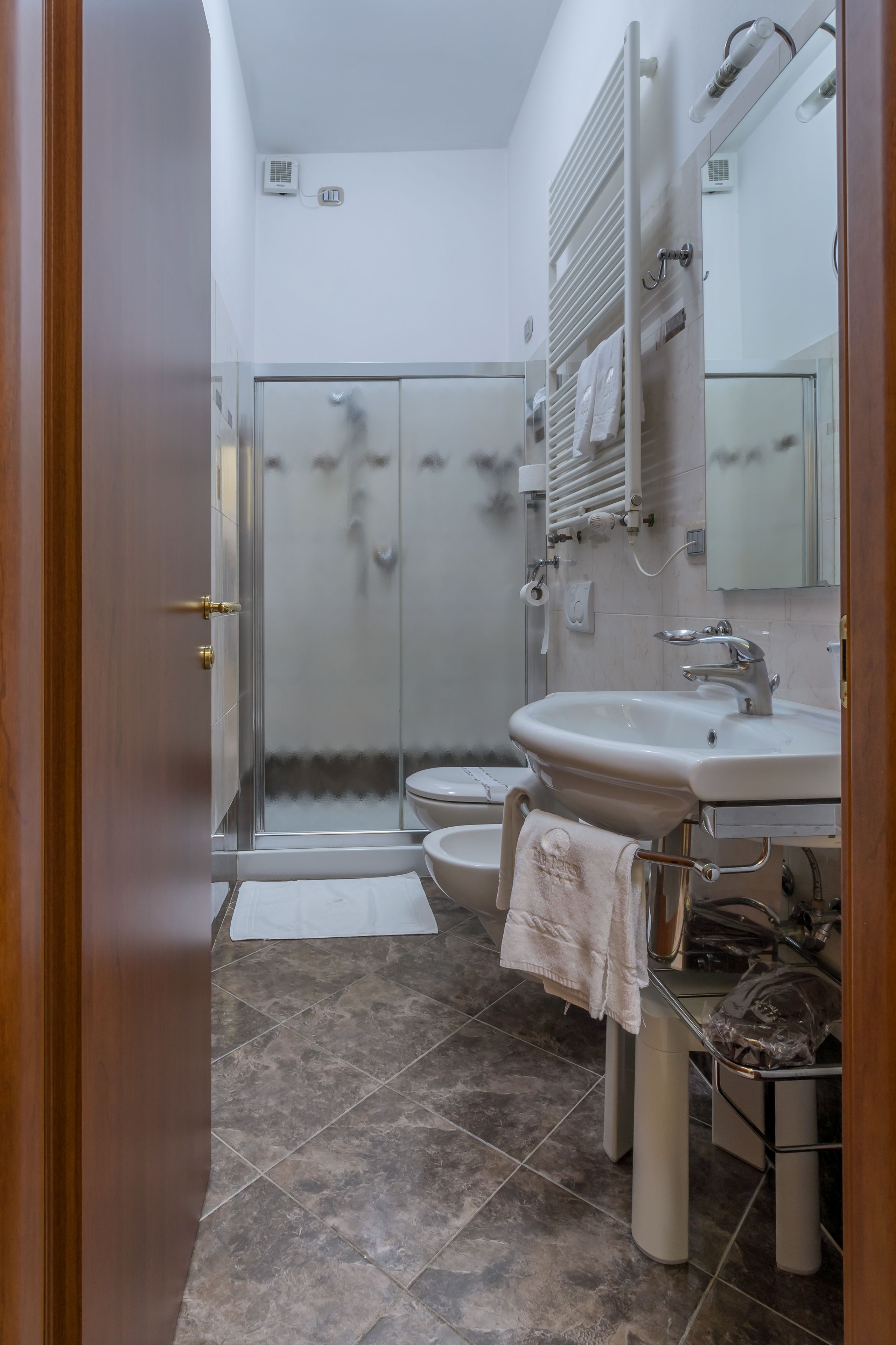 A bathroom with a glass shower enclosure, a sink with a towel, and a toilet.