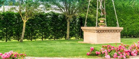 A garden with a fountain, a brick structure, and pink flowers.