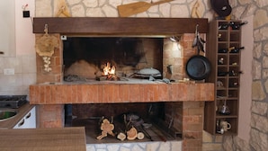 Eine Steinsäule mit Kamin, ein Ablageregál mit Flaschen und ein rustikales Holzregal mit einem Hut.