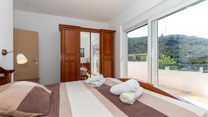 Ein Schlafzimmer mit einem großen Bett, einem Holzschrank, einem Spiegel und Blick auf eine grüne Landschaft vom Balkon aus.