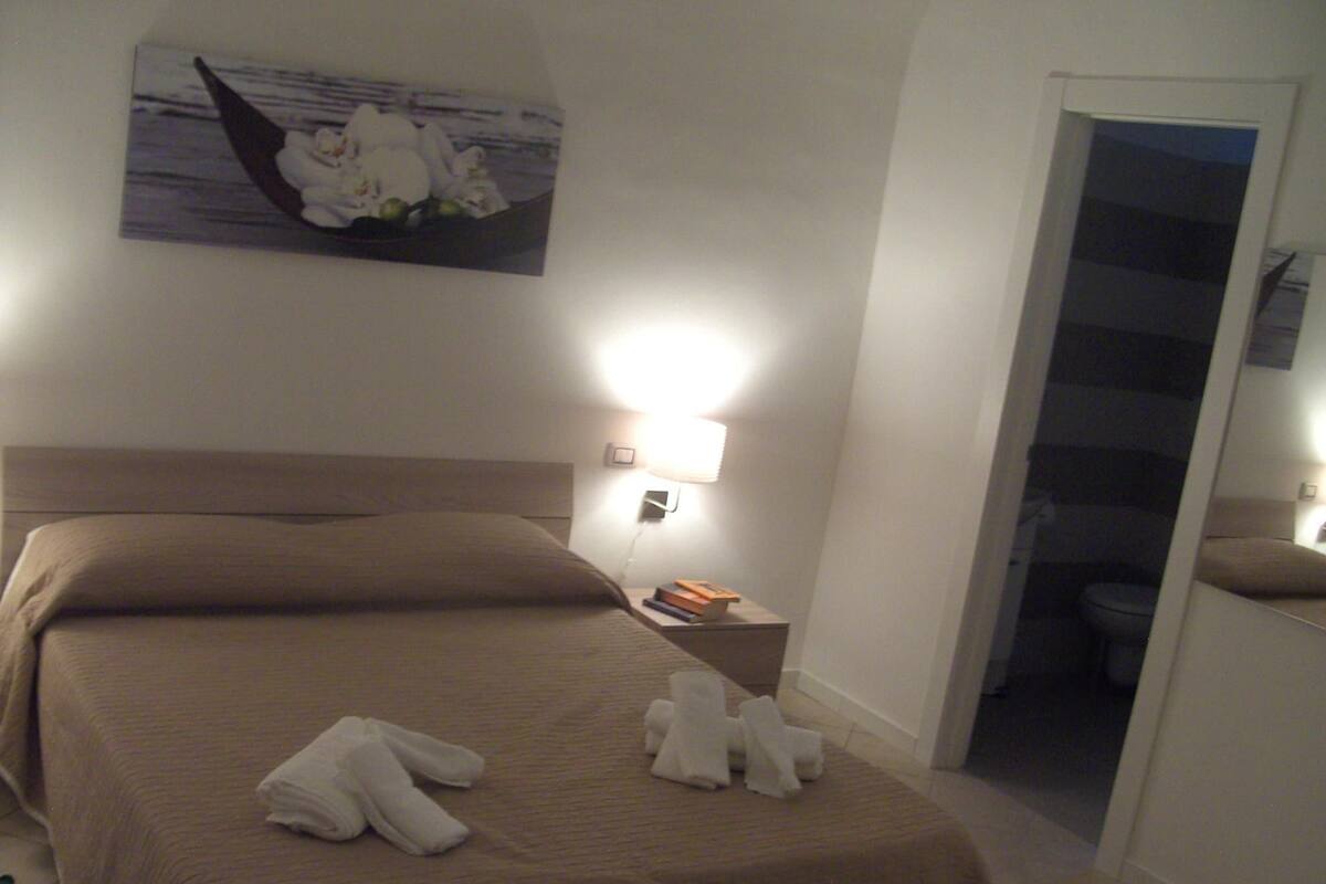 A hotel room with a bed, a nightstand, a lamp, and a painting on the wall.