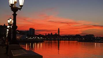 Paesaggio urbano con vista sul lungofiume al tramonto, illuminato da lampioni e con un fiume tranquillo che riflette il cielo.