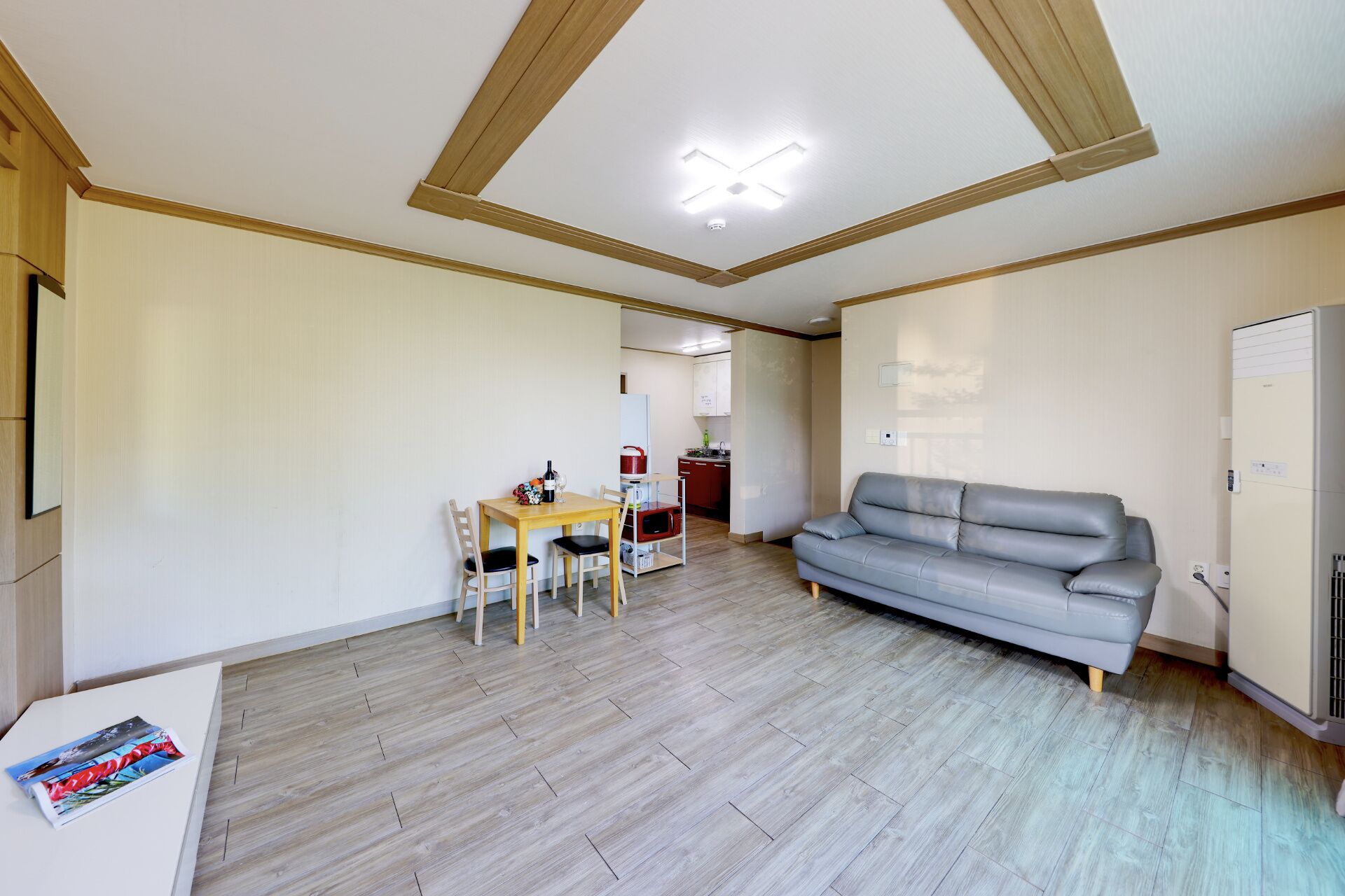 Une pièce avec un plancher en bois, un canapé gris, une table à manger en bois avec deux chaises et un coin cuisine.