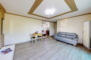 Una habitación con piso de madera, un sofá gris, una mesa de comedor de madera con dos sillas y una zona de kitchenette.