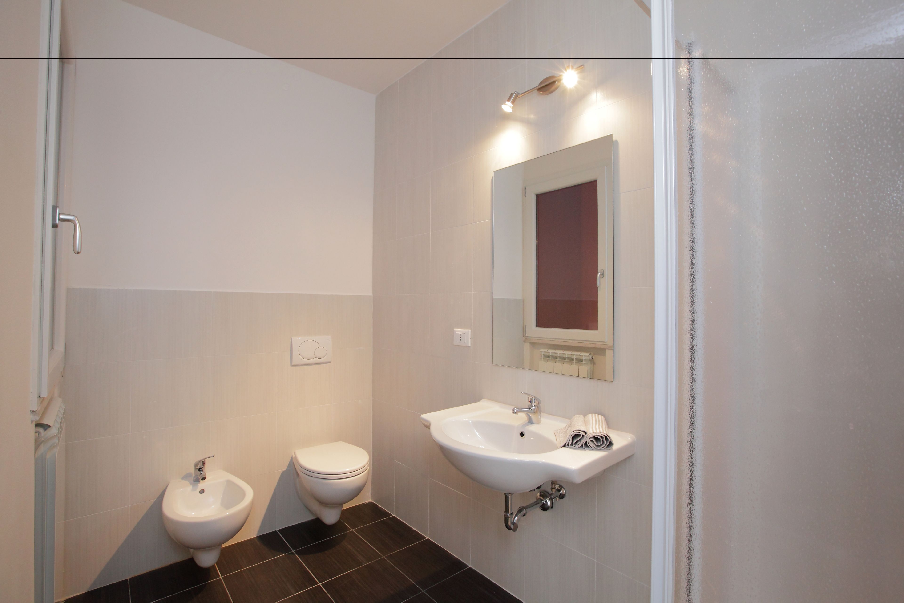 A bathroom with a bidet, toilet, sink, and mirror.