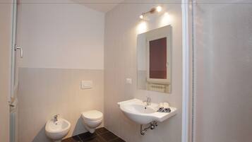 A bathroom with a bidet, toilet, sink, and mirror.