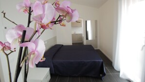 Et hotelværelse med en seng, et natbord og et stort vindue med gardiner.
