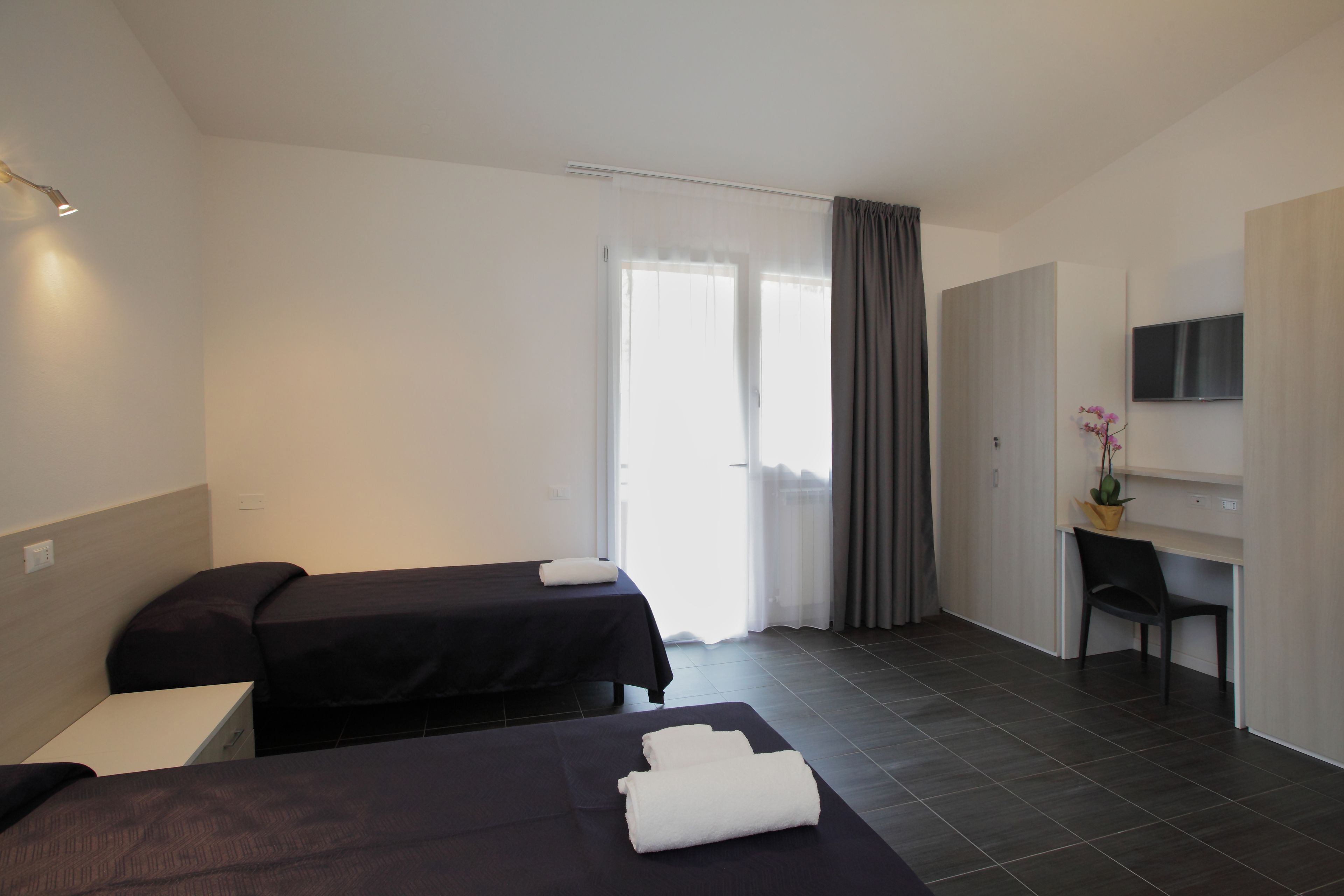 A hotel room with two beds, a desk, a chair, a TV, and a window with curtains.