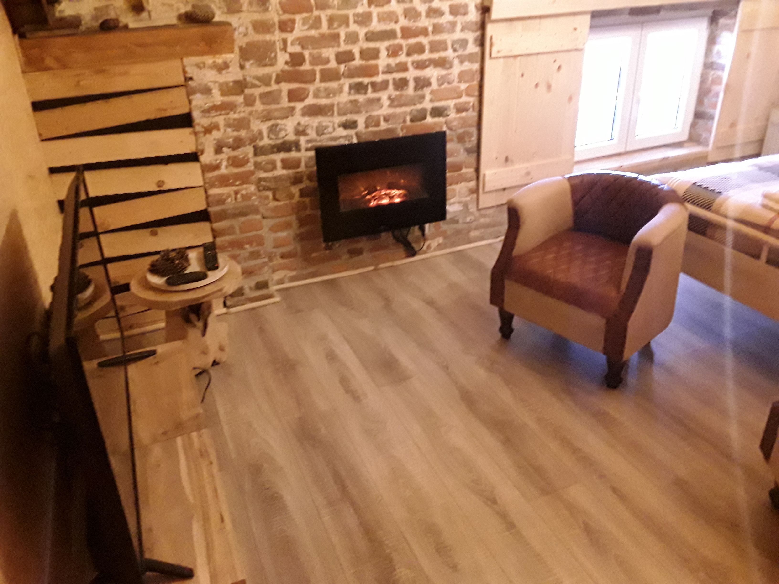 A cozy living room with a stone fireplace, a wooden staircase, and a comfortable armchair.