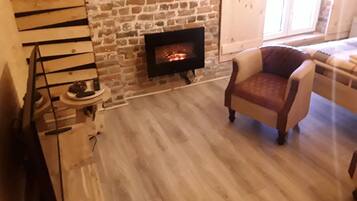 A cozy living room with a stone fireplace, a wooden staircase, and a comfortable armchair.