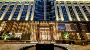 A modern hotel entrance with a water feature in front, large windows, and a sign indicating the name.