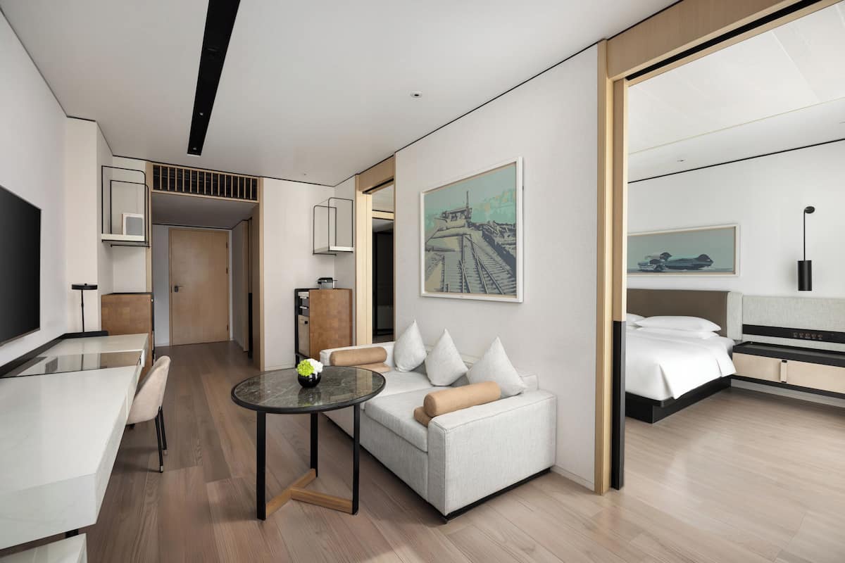 Una habitación de hotel moderna con sofá, una mesa de comedor, televisión y cama.