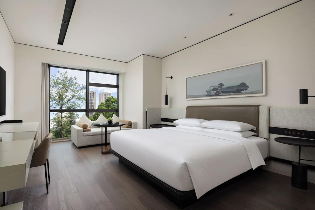 Una habitación de hotel moderna con una cama grande, un escritorio, un sofá y una ventana con vistas a la ciudad.